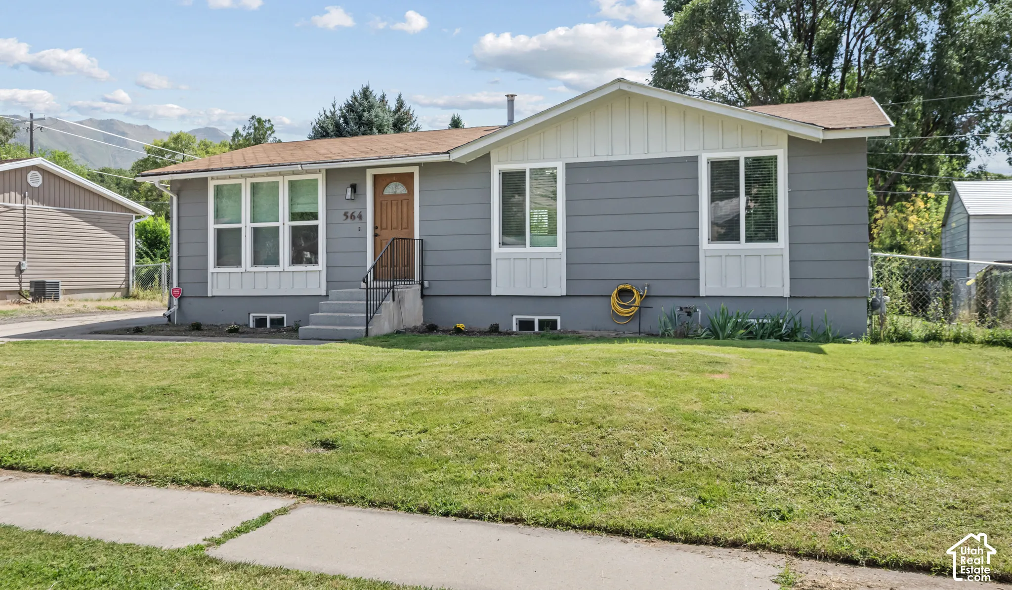 Single-story residence featuring grey siding, white trim accents, and a brown front door