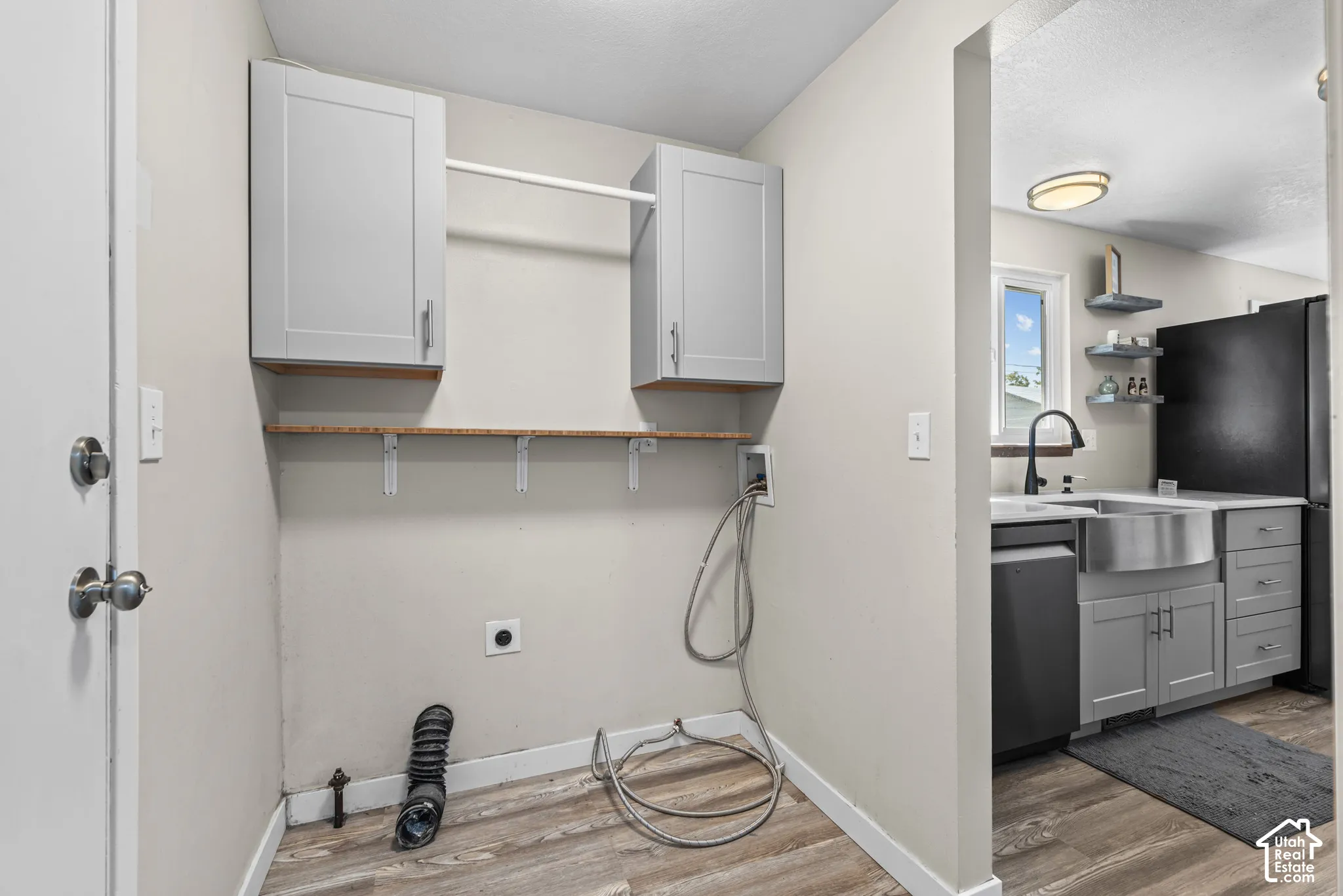 Laundry area featuring wood-finish flooring, two upper cabinets, and a hanging rod