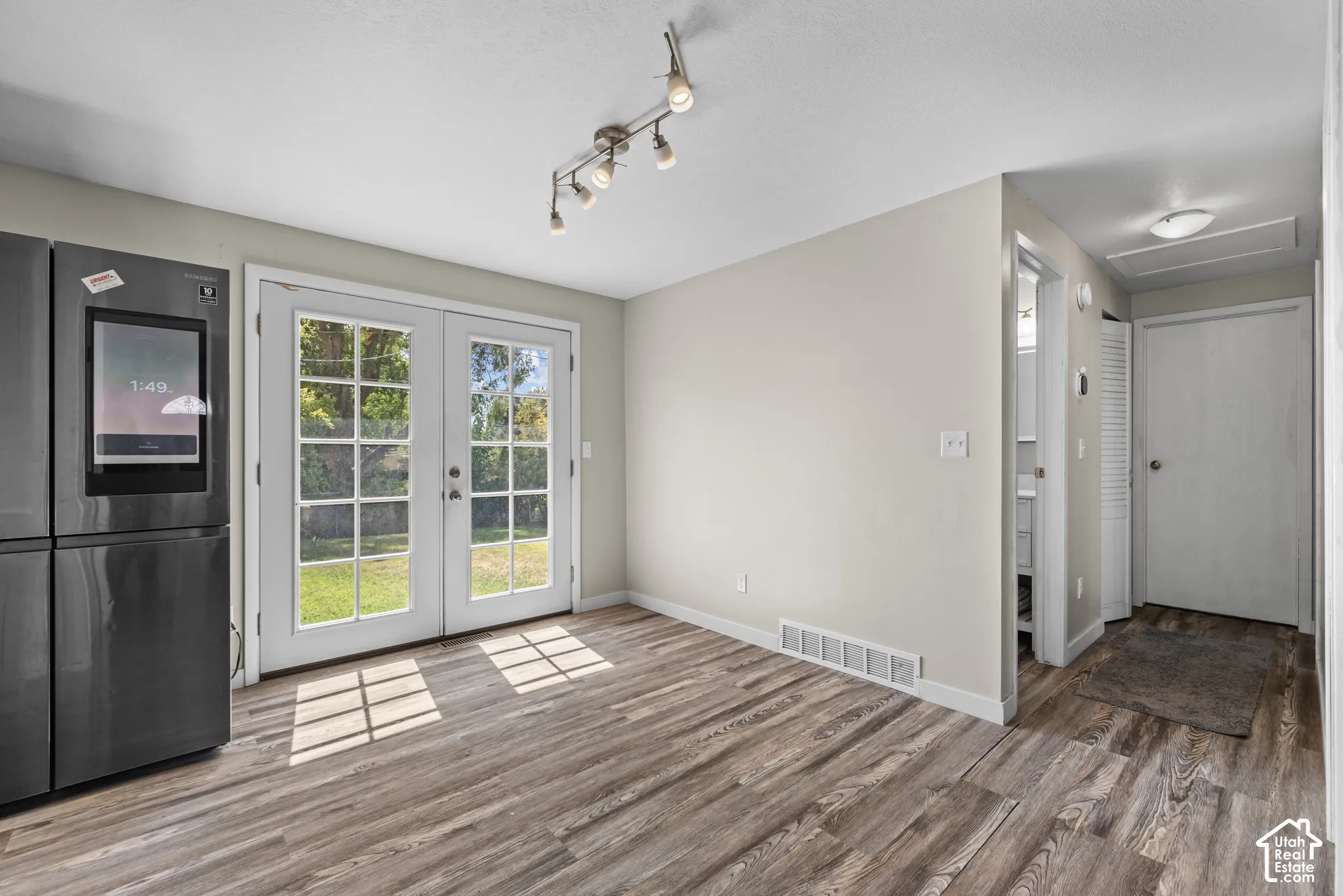Wood-finish flooring, French doors, track lighting, and a modern dark-finish refrigerator