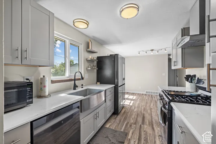 Kitchen featuring wood-finish flooring, light grey cabinetry, white countertops, a stainless steel farmhouse sink, and a stainless steel gas range with a matching hood
