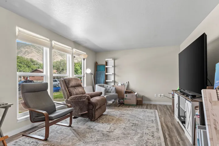 Bright living area featuring wood-finish flooring, light neutral wall tones, and multiple windows with mountain scenery