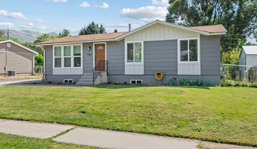 Single-story residence featuring grey siding, white trim accents, and a brown front door