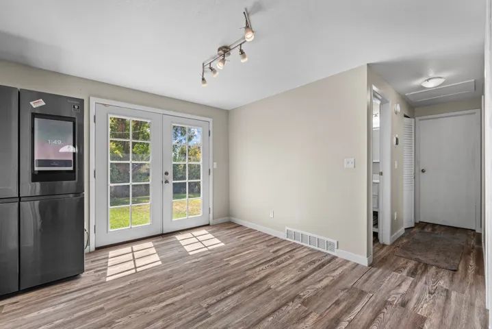 Wood-finish flooring, French doors, track lighting, and a modern dark-finish refrigerator