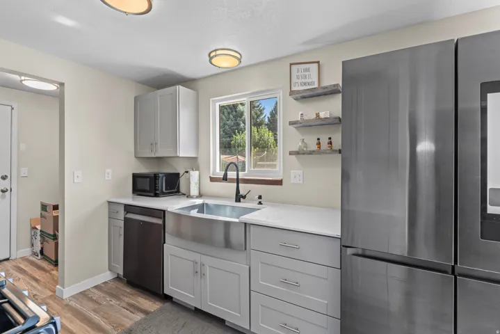 Modern kitchen with wood-finish flooring, light gray cabinetry, stainless steel farmhouse sink, and a black faucet