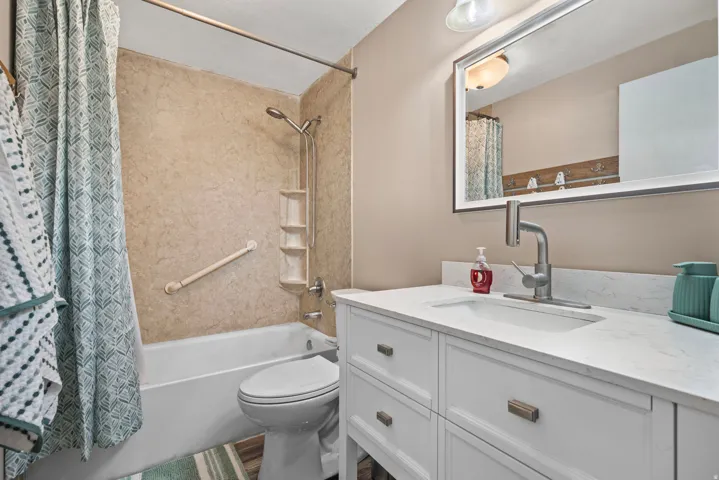 Bathroom featuring a built-in tub with a textured surround, a white vanity with an integrated sink, a wall-mounted mirror, and a contemporary brushed nickel faucet