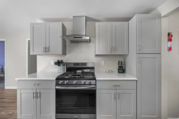 Gray shaker-style cabinetry with brushed nickel hardware, white countertops, stainless steel range, and coordinating range hood
