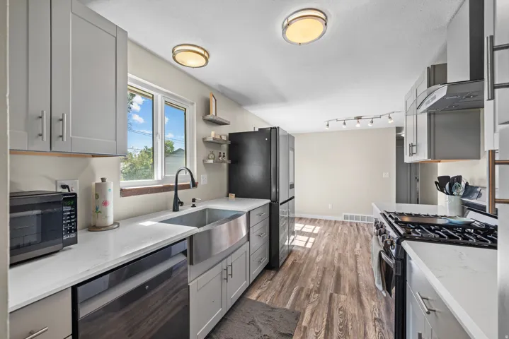 Kitchen featuring wood-finish flooring, light grey cabinetry, white countertops, a stainless steel farmhouse sink, and a stainless steel gas range with a matching hood