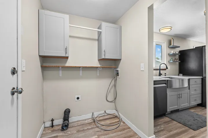 Laundry area featuring wood-finish flooring, two upper cabinets, and a hanging rod