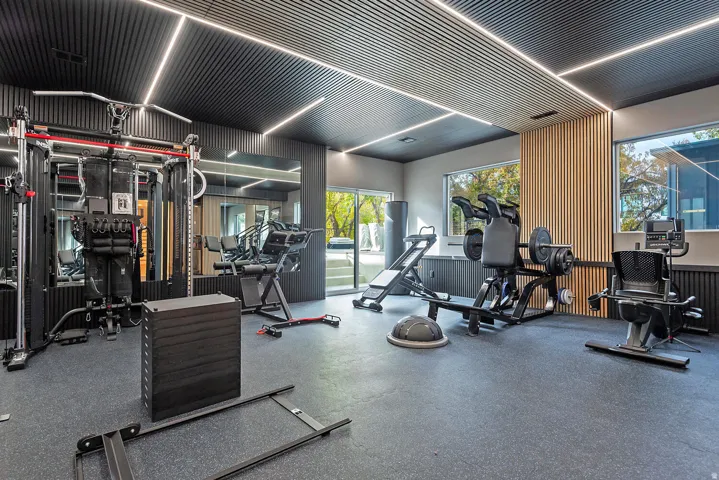 Dedicated fitness area featuring rubberized flooring, a paneled ceiling with integrated linear lighting, a mirrored wall, and floor-to-ceiling windows