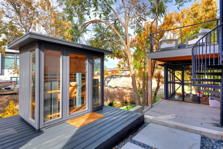 Outdoor sauna with multiple glass panels, dark composite decking, concrete patio, and a spiral staircase