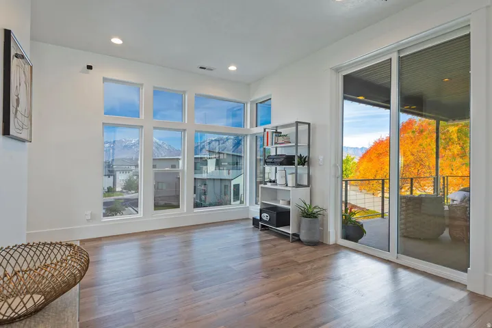 Expansive windows and sliding glass door, recessed lighting, wood-finish flooring, and a covered balcony with metal railings