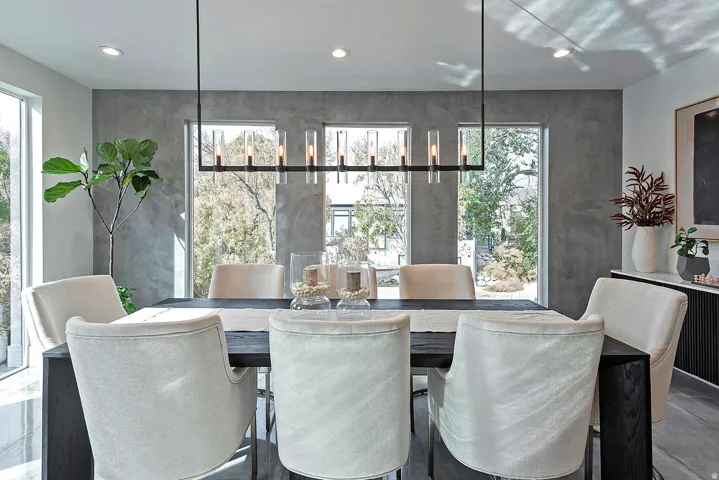 Modern linear chandelier with cylindrical glass shades, recessed ceiling lighting, and a textured accent wall