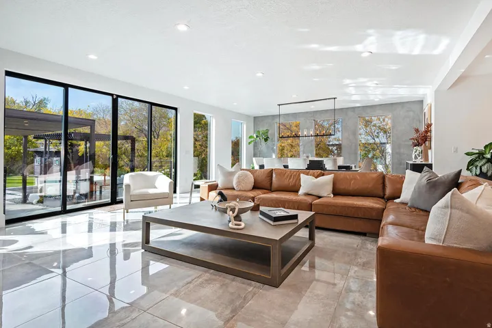 Spacious open-concept living area featuring large format tile flooring, expansive sliding glass doors, multiple recessed lights, and a linear chandelier