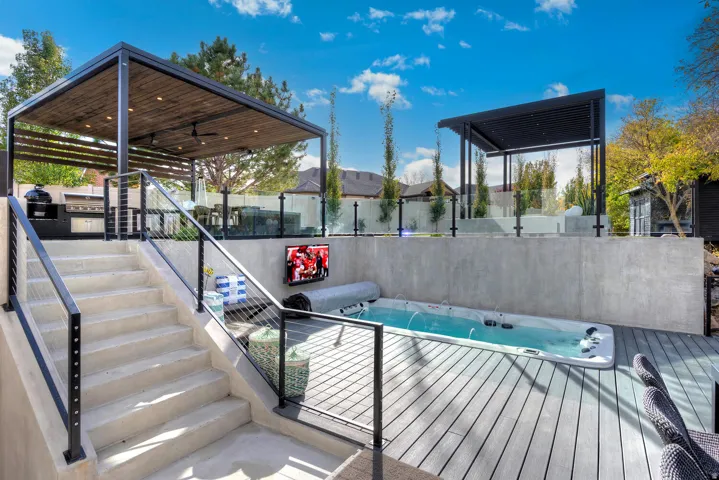 Multi-level outdoor living space featuring a swim spa, composite decking, and concrete stairs with cable railings