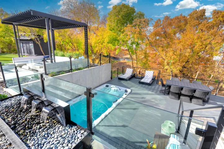 Multi-level outdoor deck featuring a built-in hot tub, black metal pergola, and glass panel railings