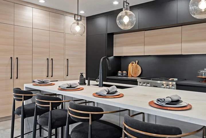 Integrated stainless steel range, light wood-finish cabinetry, dark contrasting cabinetry, white stone island countertop, and spherical pendant lighting