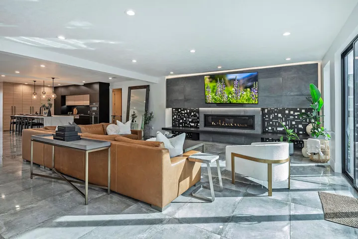 Open-concept living space featuring large format stone flooring, a linear fireplace with stone surround, recessed lighting, and a modern kitchen with integrated appliances and pendant lighting
