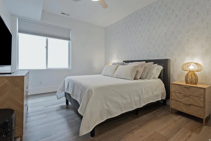 Wood-finish flooring, accent wall, ceiling fan, and large window with blinds