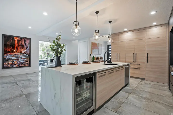 Spacious kitchen featuring a large central island with waterfall countertop, integrated beverage cooler, and pendant lighting