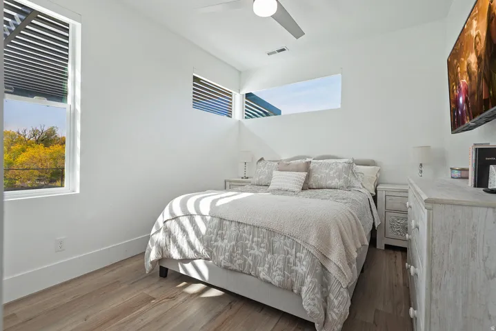 Wood-finish flooring, white walls, multiple windows, and a ceiling fan