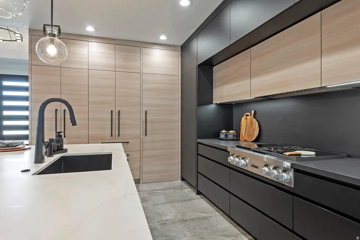 Modern kitchen featuring light wood-finish cabinetry, dark flat-panel lower cabinetry, light-toned countertop surfaces, and stainless steel range