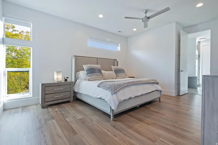Wood-finish flooring, recessed lighting, ceiling fan, multiple windows, and a doorway with a light-colored door