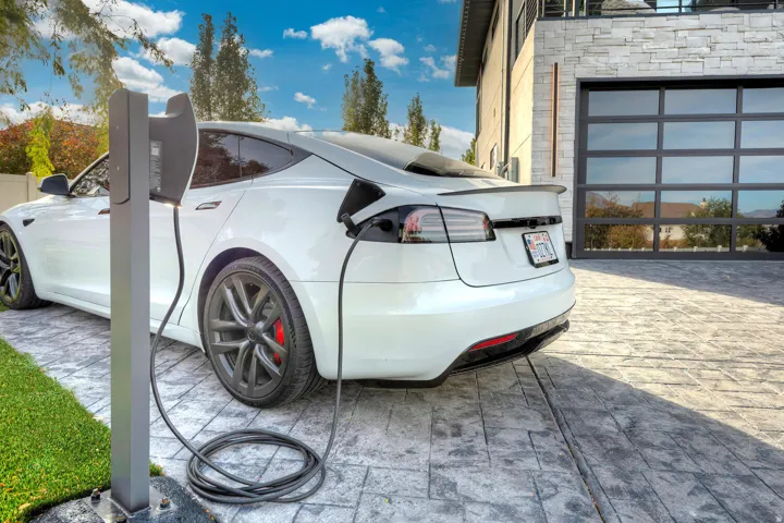 Attached charging station with stamped concrete driveway, glass panel garage door, and stone facade