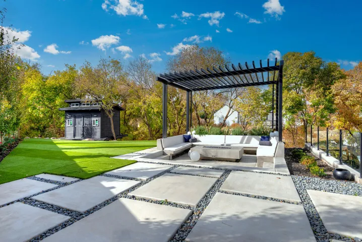Expansive patio featuring large concrete pavers, gravel accents, and a modern pergola