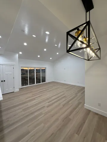 Vaulted ceiling with recessed lighting, wood-finish flooring, contemporary chandelier, and expansive sliding glass doors