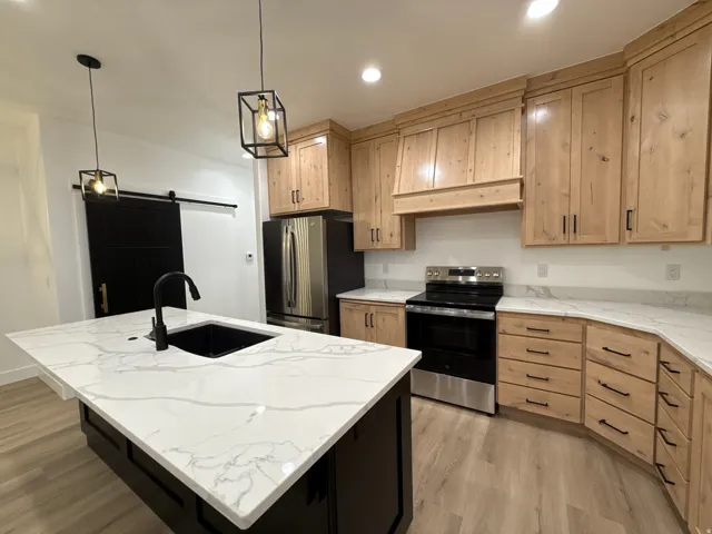 Kitchen featuring light wood-finish cabinetry, white stone countertops, stainless steel appliances, and a black barn door