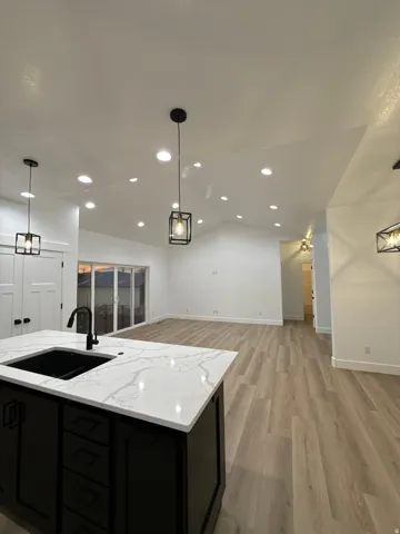 Kitchen island with a black sink and white countertop, wood-finish flooring, recessed lighting, and modern pendant fixtures