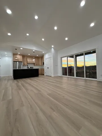 Wood-finish flooring throughout, recessed ceiling lighting, kitchen island with dark finish, sliding glass patio doors, and natural wood cabinetry