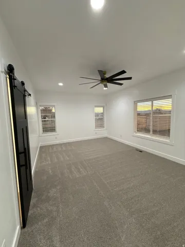 Spacious room featuring neutral carpet, multiple windows with blinds, a modern ceiling fan, recessed lighting, and a black barn door