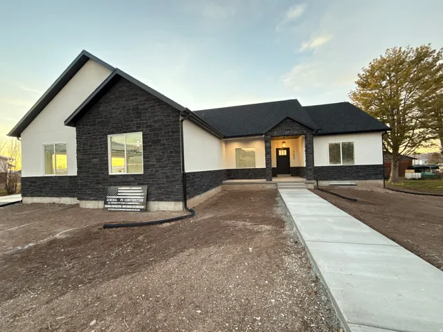 Contemporary architectural style featuring a dark stone facade and white stucco, a covered entry with an exterior light fixture, a black front door, a dark asphalt shingle roof, and a concrete walkway