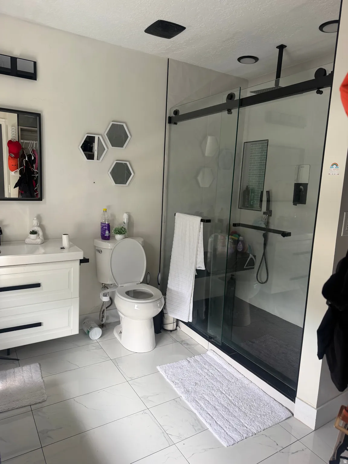 White tiled flooring with a dark-framed sliding glass shower enclosure, white vanity, and a ceiling-mounted showerhead