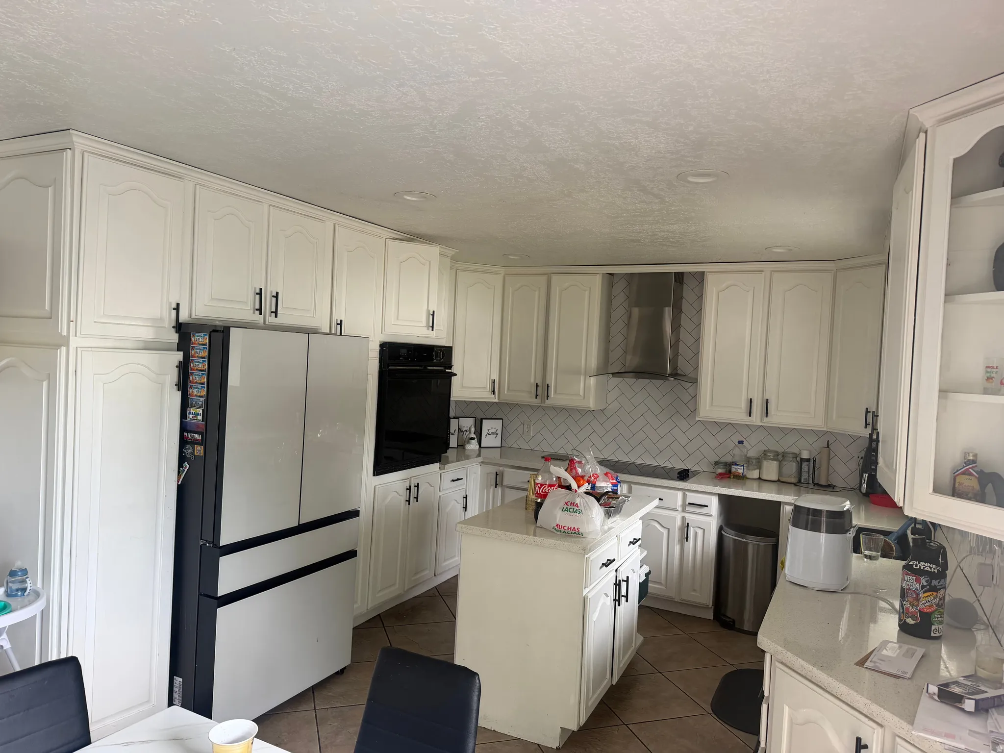 White cabinetry with black hardware, white countertops, herringbone tile backsplash, stainless steel range hood, and recessed lighting