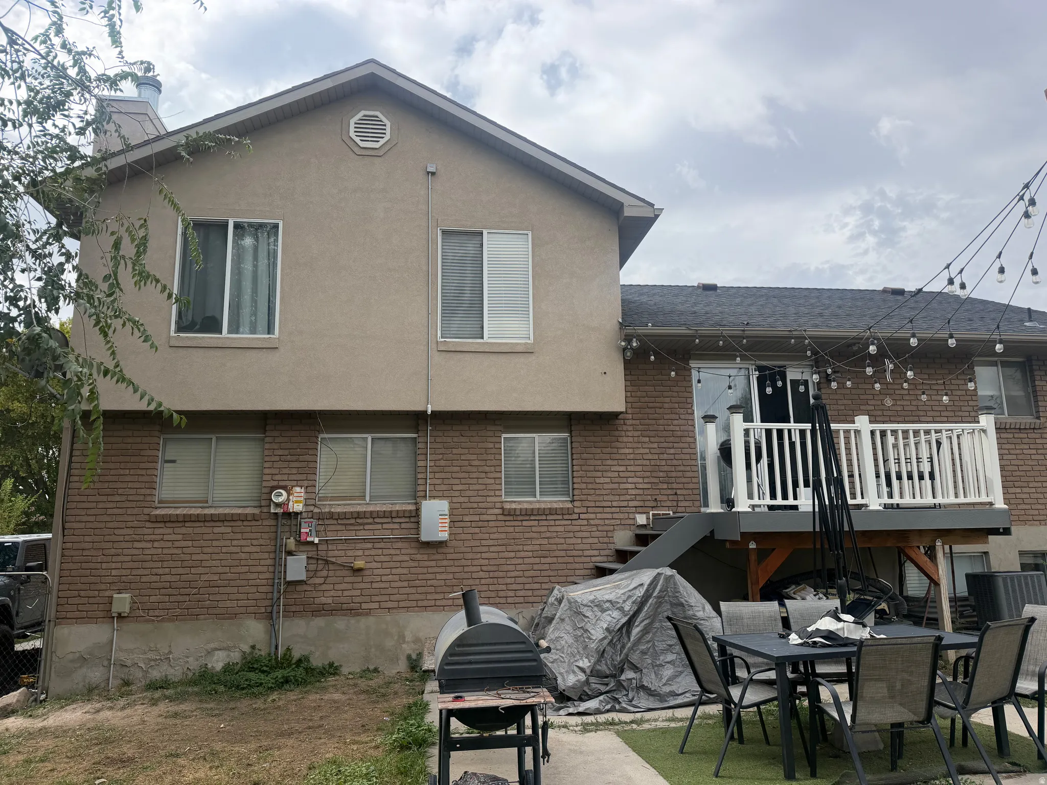 Two-story exterior featuring a brick and stucco facade, upper-level deck with white railing, and a ground-level patio area with artificial turf