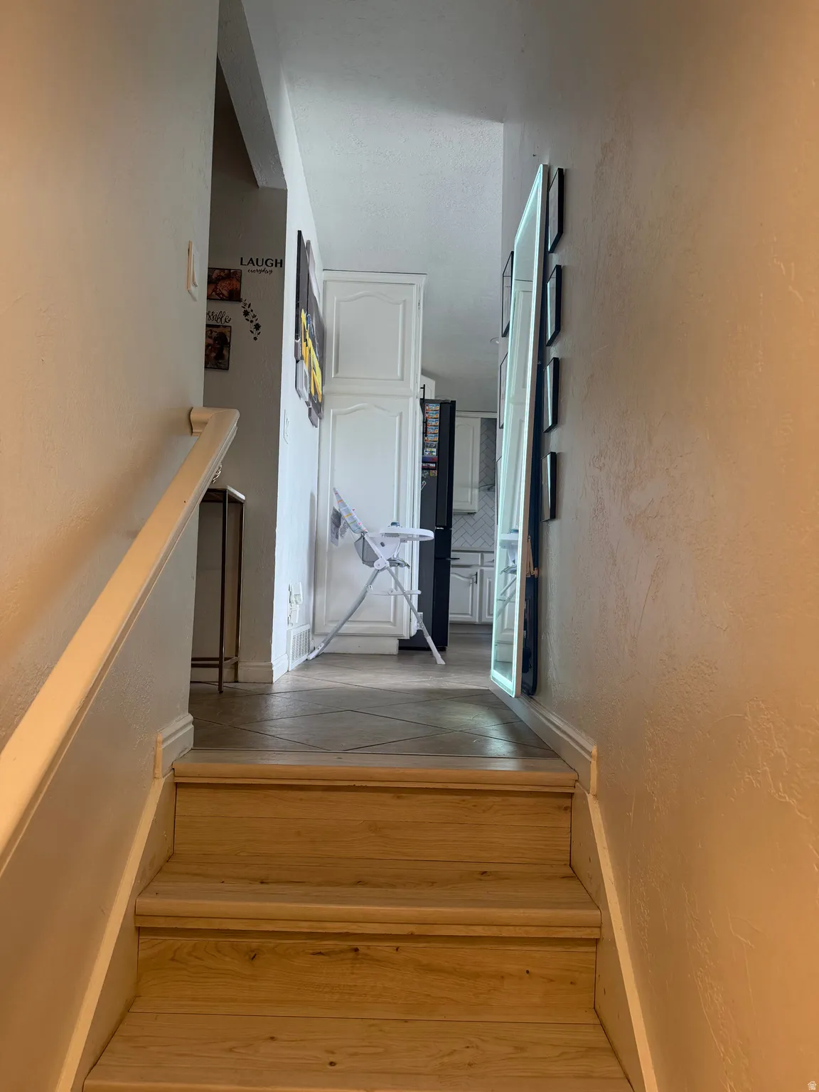 Wood-finish staircase with white painted handrail, leading to a tiled landing