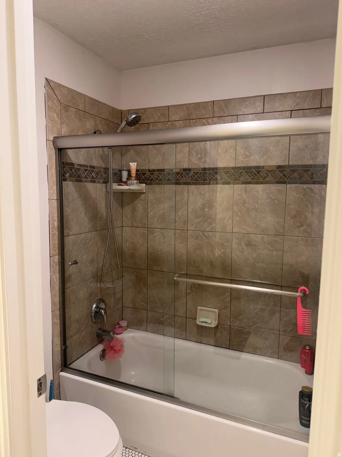 Bathtub with sliding glass enclosure, tile surround with decorative accent band, and chrome fixtures