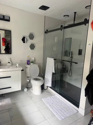 White tiled flooring with a dark-framed sliding glass shower enclosure, white vanity, and a ceiling-mounted showerhead