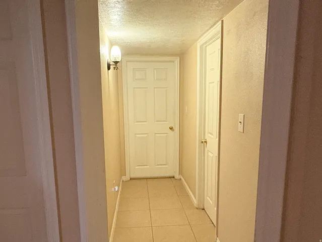 Hallway featuring tile flooring, neutral wall tones, white paneled doors, and wall-mounted lighting