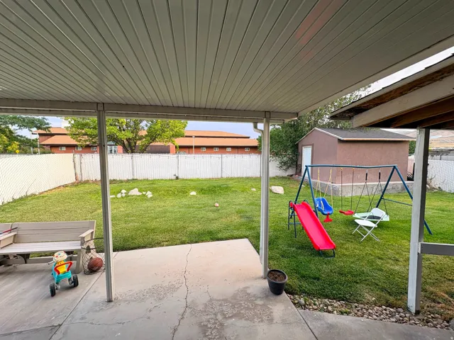 Covered patio with concrete flooring, chain link fencing, and a detached storage shed