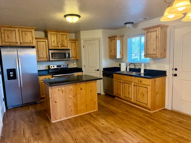 Kitchen featuring natural wood cabinetry, dark countertops, stainless steel appliances, a central island, and wood-finish flooring