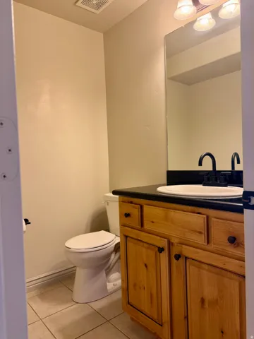 Wood-finish vanity with a dark countertop, white oval sink, and matte black faucet