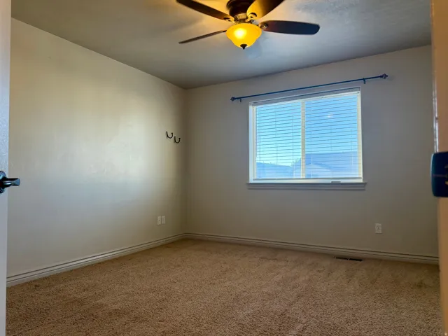 Carpeted primary bedroom, window with blinds, ceiling fan with light fixture, and wall-mounted hooks