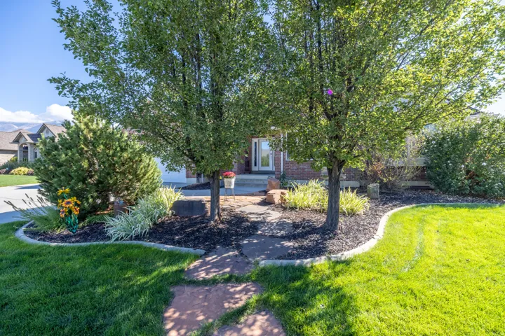 Manicured front yard with mature trees, established landscaping, and a paver stone pathway