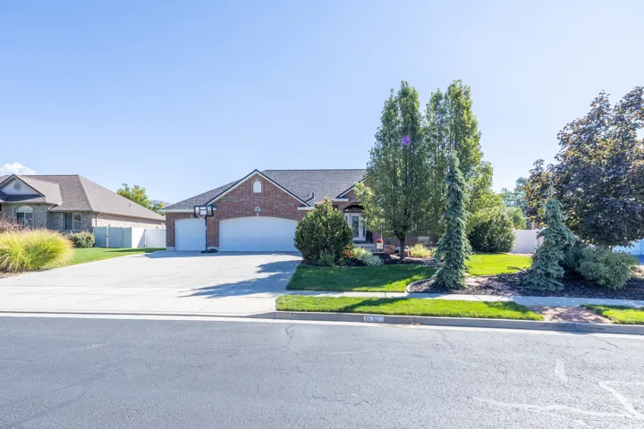 Brick exterior with a three-car garage, concrete driveway, and mature landscaping