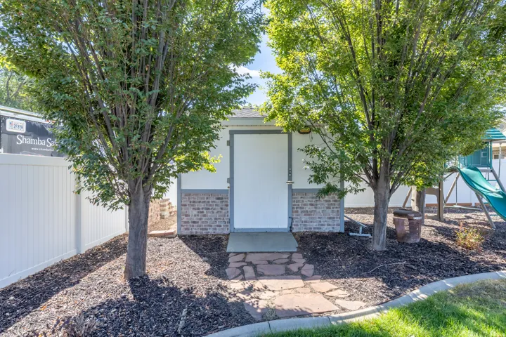 10' X12' Storage shed with brick-finish skirting and a white door, framed by two mature trees