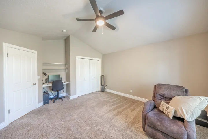 Vaulted ceiling with a ceiling fan, built-in desk with shelving, bi-fold closet doors, and neutral carpeting