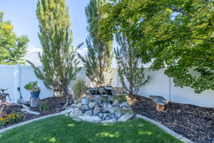 A stone waterfall feature, mature trees, and a white privacy fence